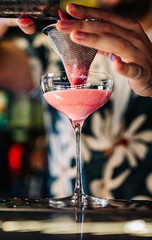 man hand bartender pouring pink cocktail in glass on the bar counter