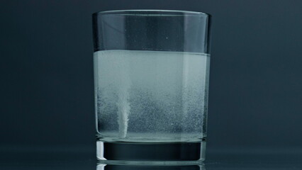 White pill dissolving glass at dark background closeup. Effervescent tablet flow