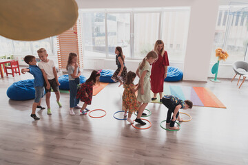 Small nursery school children with female teacher on floor indoors in classroom, doing exercise....