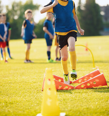 School Boy Running Slalom Track Between Training Poles and Jumping Over Cones. Teenage Football Players Running on Training Camp. Soccer Training Equipment