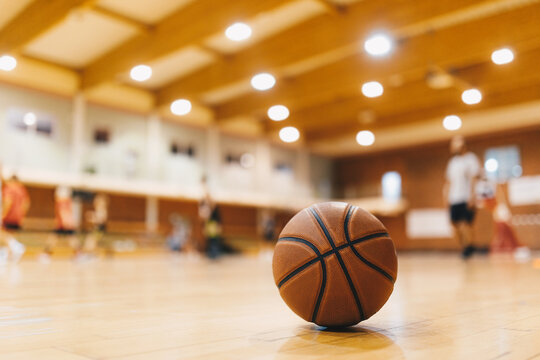 Basketball Training Game Background. Basketball on Wooden Court Floor Close Up with Blurred Players Playing Basketball Game in the Background. © matimix