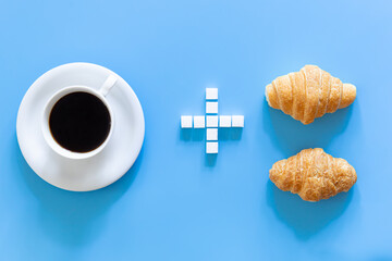 A cup of coffee, a plus sign made of sugar, and a croissants, flat lay.