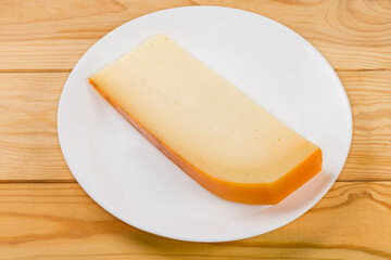 Piece of semi-hard cheese on dish on rustic table