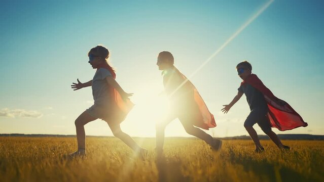 team superhero. a group of children are running across the field in a superhero costume with a silhouette of a red cape at sunset. the concept of a happy family dream childhood. teamwork superhero