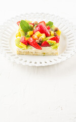 Top view of fruit tart on white plate, white table, vertical, with copy space