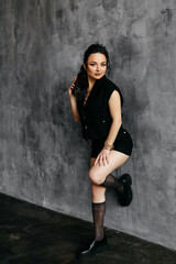 A beautiful young brunette woman with makeup in fashionable and trendy clothes poses against a black and gray isolated wall. Sexy model laughs and looks at the camera. Selective focus