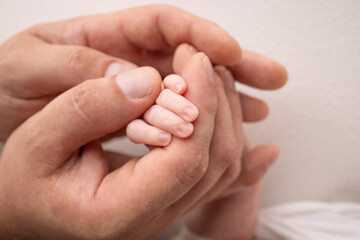 A newborn holds on to mom's, dad's finger. Hands of parents and baby close up. A child trusts and holds her tight. Tiny fingers of a newborn. The family is holding hands. Concepts of family and love.