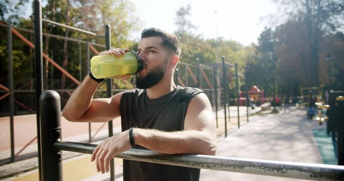 Healthy lifestyle and outdoor training. Athletic man drinking water after grueling cardio. Young aspiring bodybuilder resting after warm-up. End of workout, good job. Sports and fitness technology.