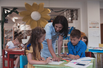 Creative kids during an art class in a daycare center or elementary school classroom drawing with female teacher. 