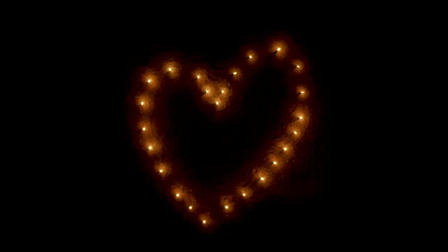 Heart made out of burning torches on beach at night, aerial zoom out.