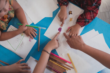 Creative kids during an art class in a daycare center or elementary school classroom drawing with female teacher. 