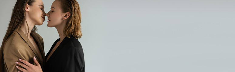 side view of pretty lesbian couple in jackets standing face to face isolated on grey, banner.
