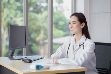 Fototapeta na wymiar Asian professional young smiling woman doctor sitting look forward in office at hospital. On table has a paper and computer.