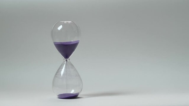 Close up of the sand clock with purple sand running down on the white wall background. Macro shooting