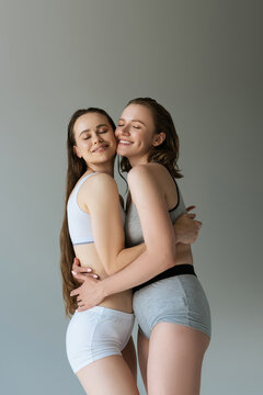 happy same sex lesbian couple in underwear embracing with closed eyes isolated on grey.