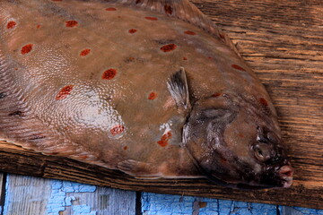 Fresh sea fish plaice (Pleuronectes platessa) on a wooden board decorated with onions, garlic and...