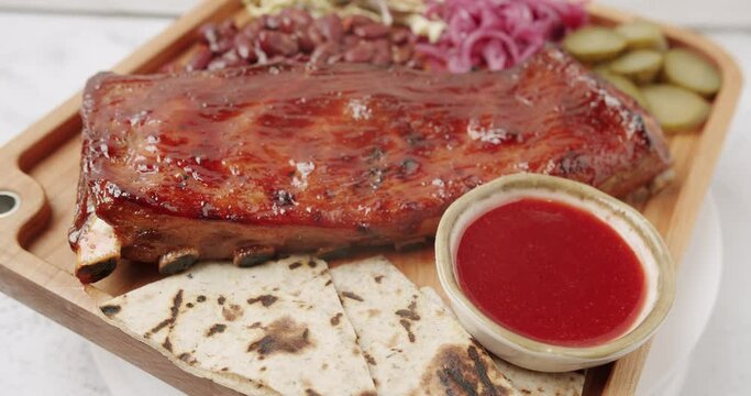 A large Plate that includes Baby Back Ribs with cherry chipotle sauce. cooked slowly on smoker, sauce, BBQ beans, coleslaw, pickled onions, pickled cucumbers, Rotating on isolated white background