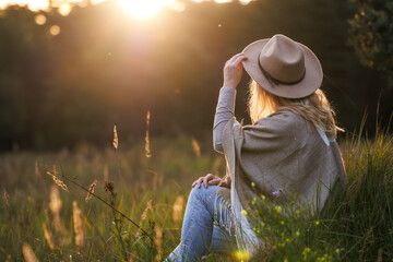 Happy woman with hat relaxing outdoors during sunset. Mental wellbeing
