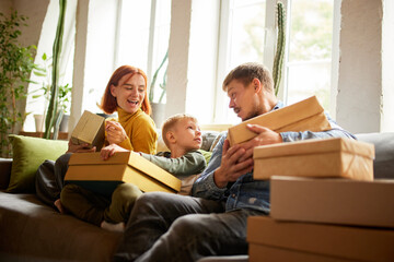 Young happy family, parents and kid received an online order, makes unpacking purchases at home. Black Friday or cyber Monday, comfort, technology concept