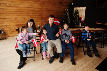 Fototapeta premium Family with Denmark flags inside wooden house sitting by table. Travel to Scandinavian countries. Happiest danish people's .