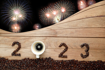 Coffee beans and hot fresh coffee in a white cup with foam and text 2023 for Happy New Year Concept. with fireworks background.