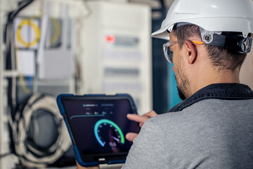 Man, an electrical technician working in a switchboard with fuses, uses a tablet.