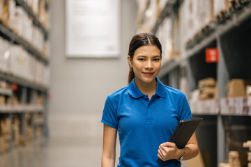 Young female worker in blue uniform checklist manage parcel box product in warehouse. Asian woman employee holding tablet working at store industry. Logistic import export concept.