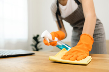 Housewife with rubber gloves and apron with spray bottle and microfiber towel to clean table at...