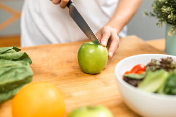 Hand of slicing and cooking green apple on cutting board for vegetable salad in weight loss diet. Beautiful woman happily cooks a healthy breakfast in kitchen in the morning. Diet food concept.