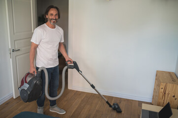 Fototapeta na wymiar Man in white tshirt doing vacuum cleaning and looking involved