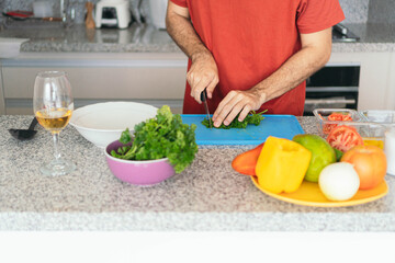 Young man chopping vegetables on a cutting board while preparing a healthy meal in his kitchen at home