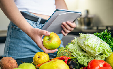 Woman with notepad and vegetables on the kitchen table preparing a recipe.