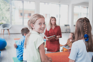 Reading time in an elementary school or kindergarten, a teacher reads a book to children in an elementary school or kindergarten. The concept of pre-school education. Selective focus