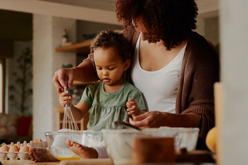 Fototapeta na wymiar Biracial mother and daughter whisking eggs together in kitchen at home