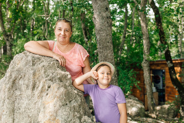 Naklejka na ściany i meble Adult mother and school aged daughter resting together in forest camp. Happy family walk and spend summer vacation in wild nature in mountains. Hiking along stone road, trip, active life.