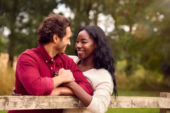 Loving Mixed Race Couple Leaning On Fence On Walk In Countryside