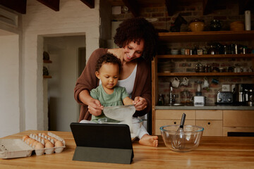 Fototapeta na wymiar Biracial mother making food with daughter by digital tablet in kitchen at home