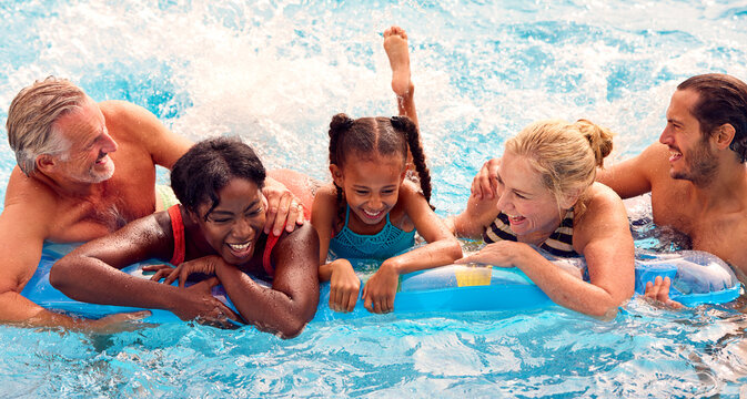 Smiling Multi-Generation Family On Summer Holiday Relaxing In Swimming Pool On Airbed
