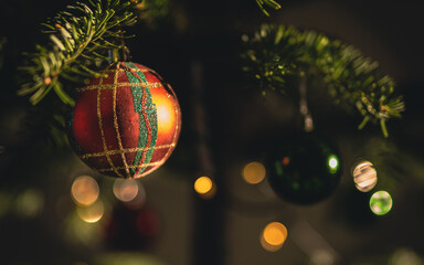 Fototapeta Boże Narodzenie kartka z bombką choinkową. Bombka choinkowa w klasycznych świątecznych kolorach zawieszona na choince. Dekoracja na ciemnym tle z efektem bokeh. obraz