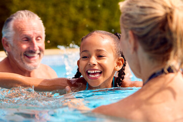 Grandparents Teaching Granddaughter To Swim On Family Summer Holiday In Pool