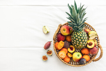 Pineapple and other exotic fruits in a basket on a white background, top view.