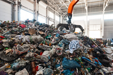 Excavator grabs trash in warehouse of waste processing plant - Powered by Adobe