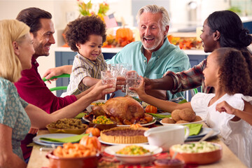 Multi-Generation Family Celebrating Thanksgiving At Home Eating Meal And Doing Cheers With Water