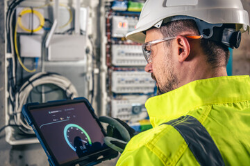 Man, an electrical technician working in a switchboard with fuses, uses a tablet.