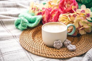 Home composition with a cup of coffee, flowers and a knitted element.