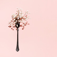 Black painted vintage style fork and tiny white flowers, creative arrangement on pastel pink background. 
