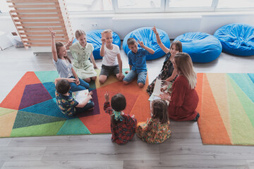 A happy female teacher sitting and playing hand games with a group of little schoolchildren