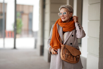 Smiling Woman Outdoor Portrait. Short blonde hair fashion model wears stylish clothes, double-breasted jacket, leather handbag, ochre knitted scarf and glasses. Fashion trend of autumn or spring - obrazy, fototapety, plakaty
