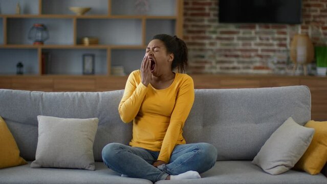 Seasonal apathy. Young african american woman yawning on sofa at home, feeling tired and exhausted, empty space