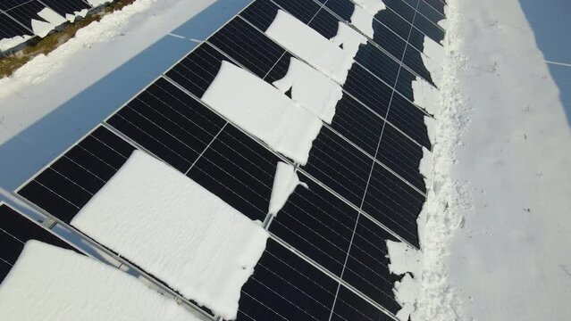 Aerial view of snow melting from covered solar photovoltaic panels at sustainable electric power plant for producing clean electrical energy. Low effectivity of renewable electricity in winter